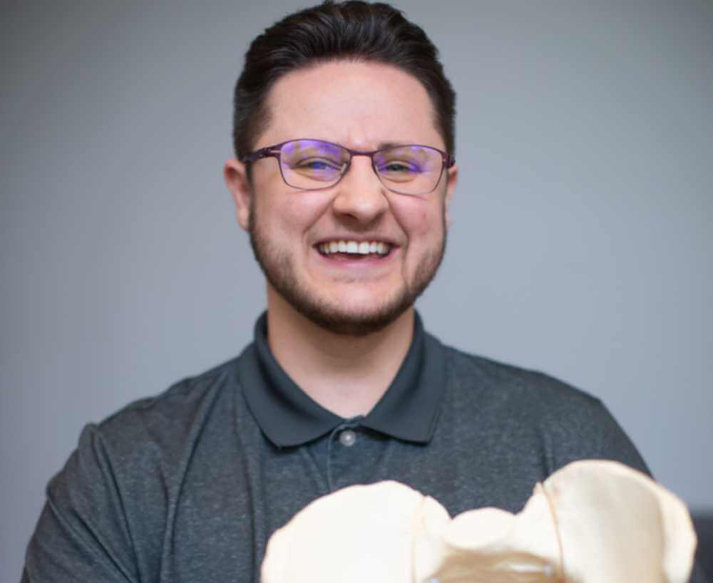 Photo of Ken McGee smiling and holding a model pelvis.